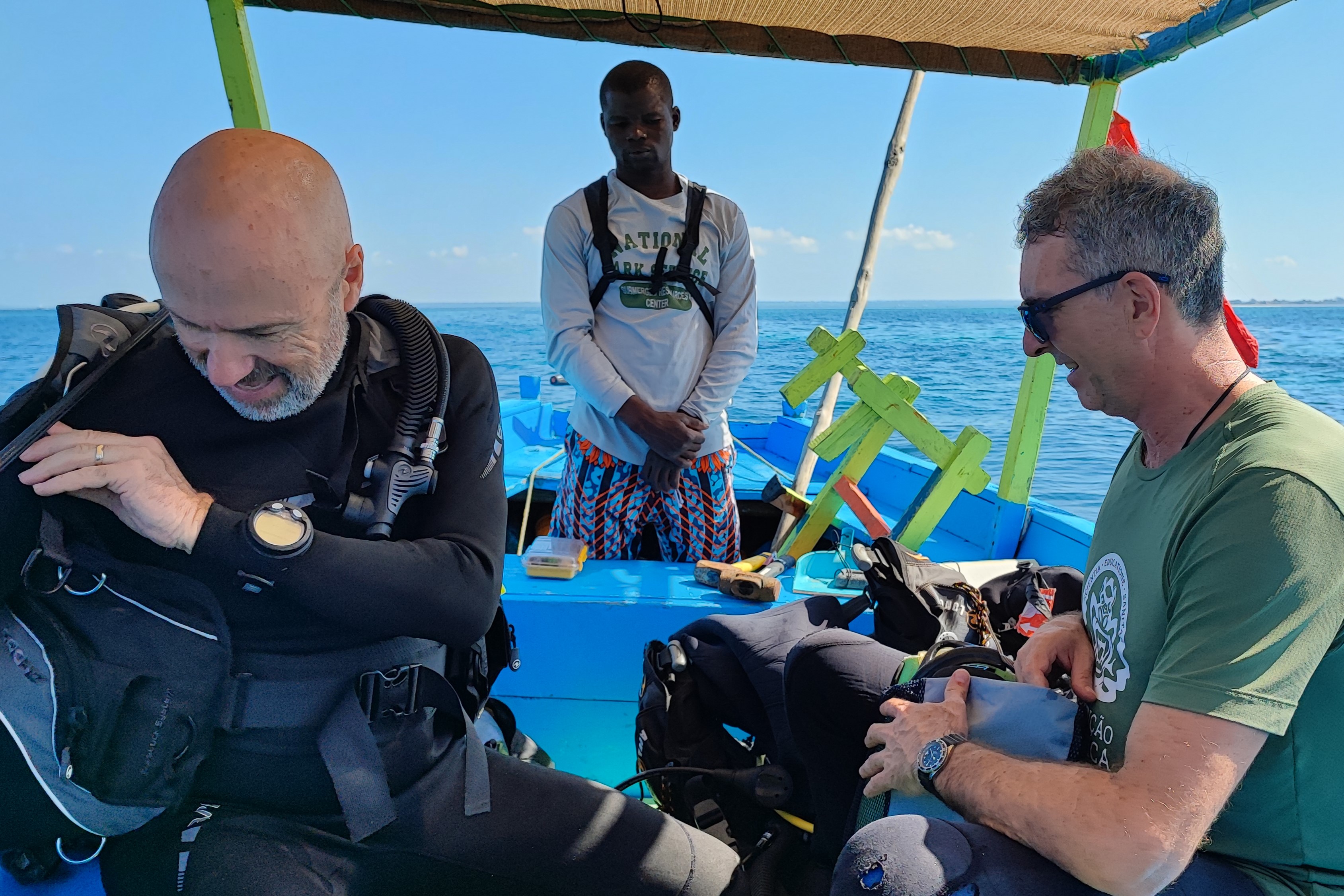 three men putting on scuba gear at the back of a boat
