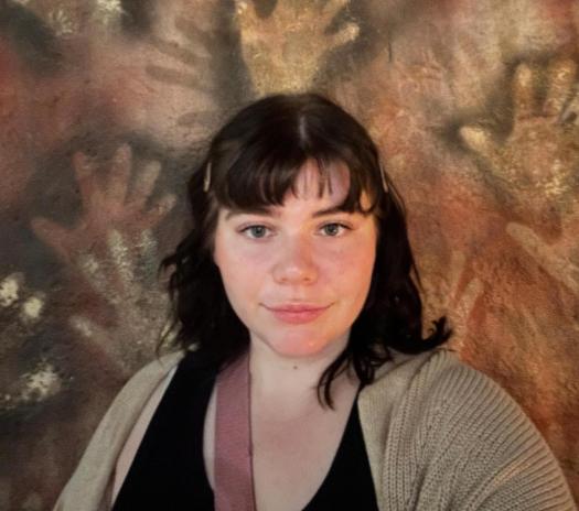 Sarah Bender is a White woman with dark hair standing against a background of cave art handprints.