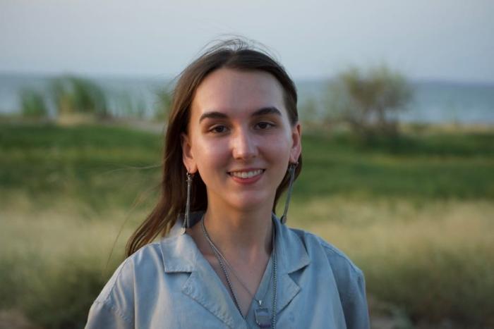 Alison is a White woman with dark hair wearing a blue shirt. She stands against a rural background.