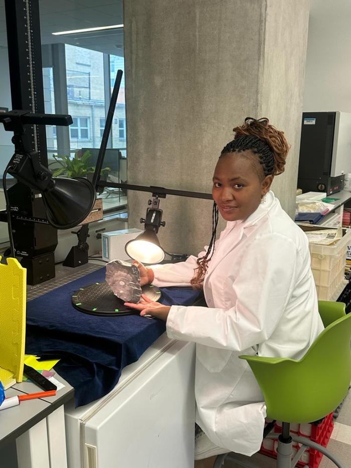 Joyce is a Black woman wearing lab PPE in a lab setting.