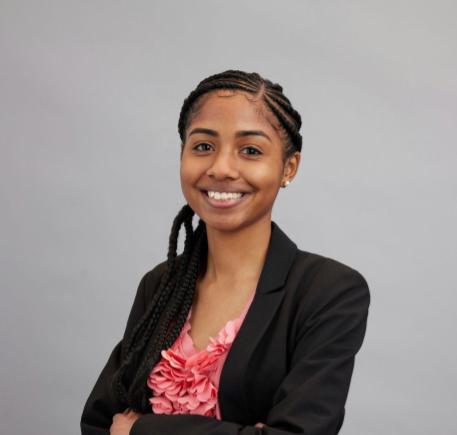 Kaija Harlow is a Black woman wearing a black blazer and a pink, floral shirt.